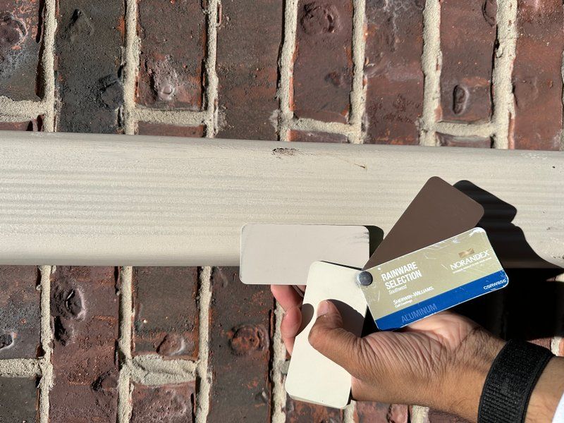 Holding aluminum gutter color swatches against a brick wall to find the right match